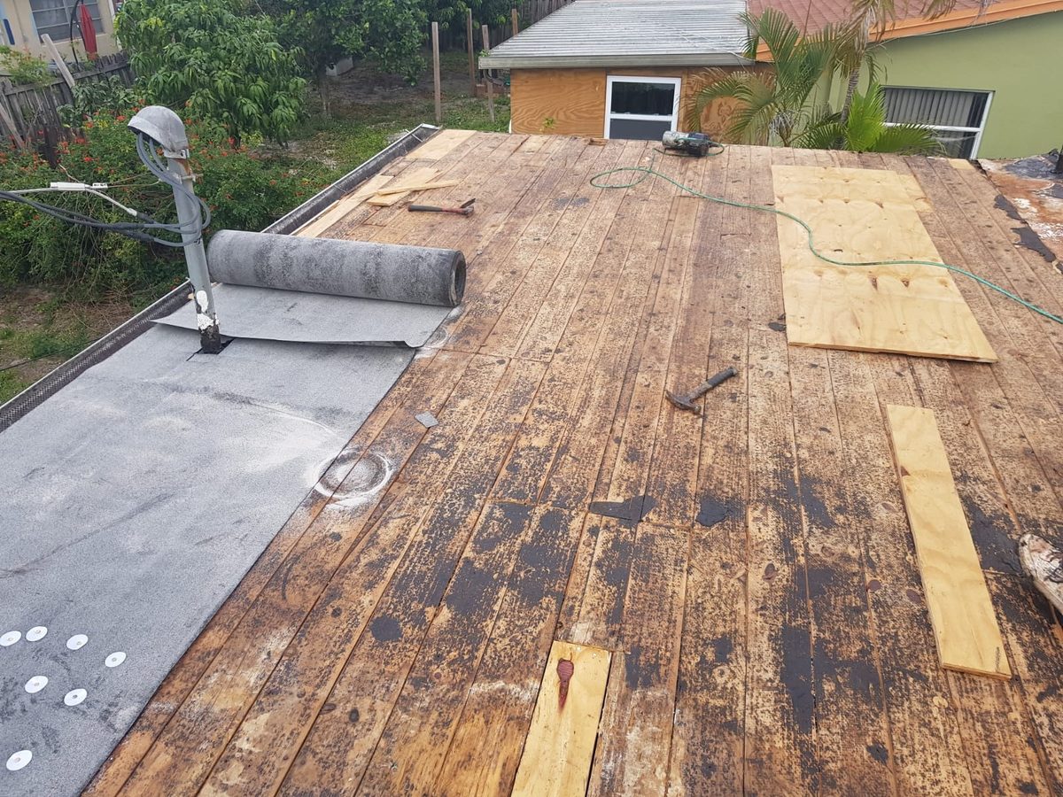 An in-progress roof replacement showing exposed wood decking and a roll of underlayment.