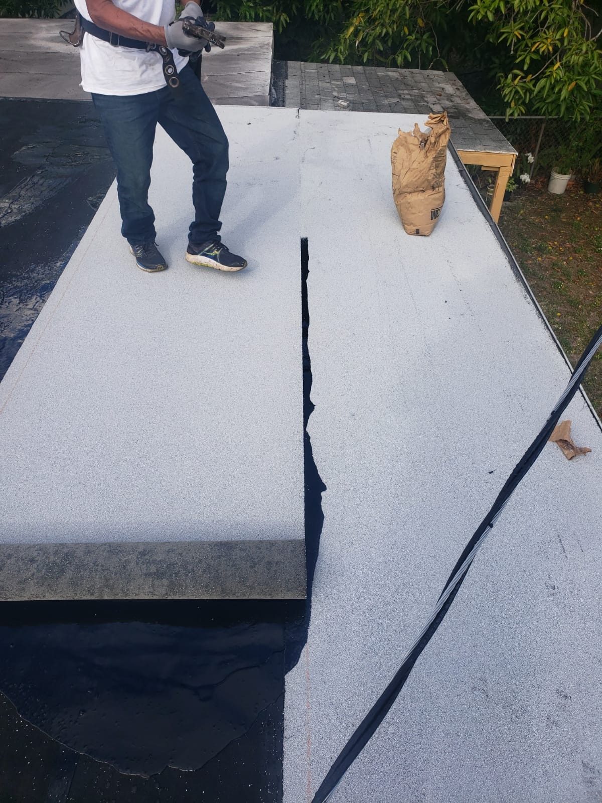 A worker standing on a flat roof during the installation of a white roll roofing membrane.