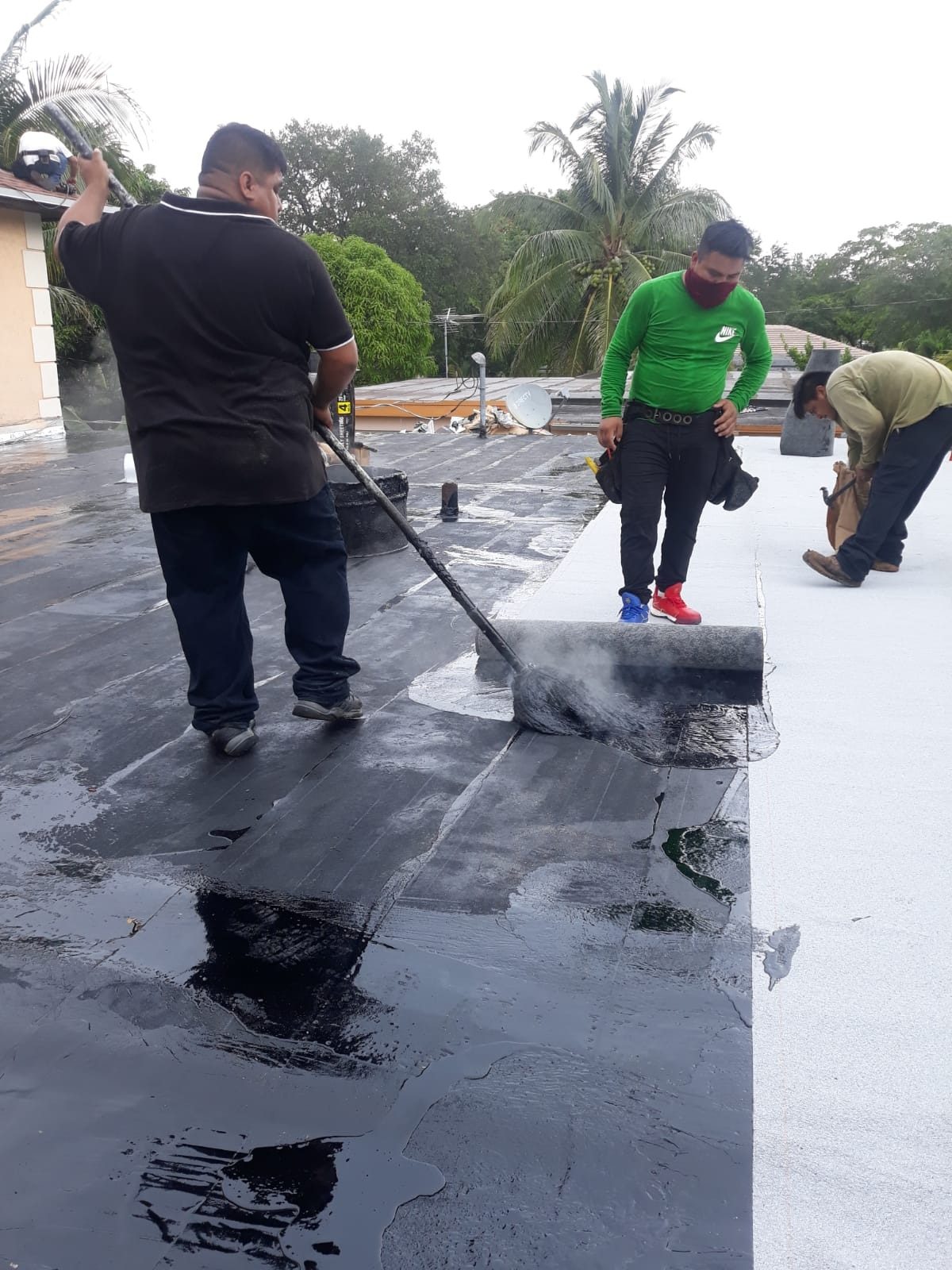 Roofers working on a flat roof applying a black liquid coating.