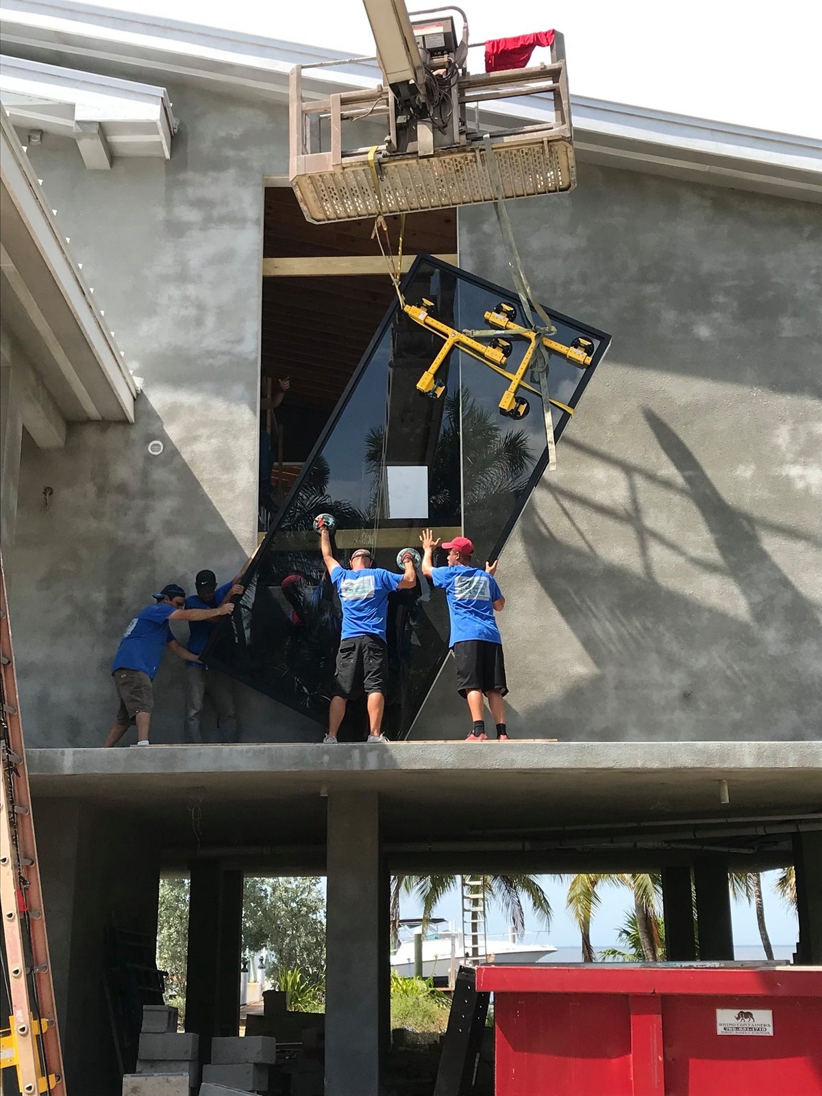 Workers guiding a large glass window pane into place on a concrete building.