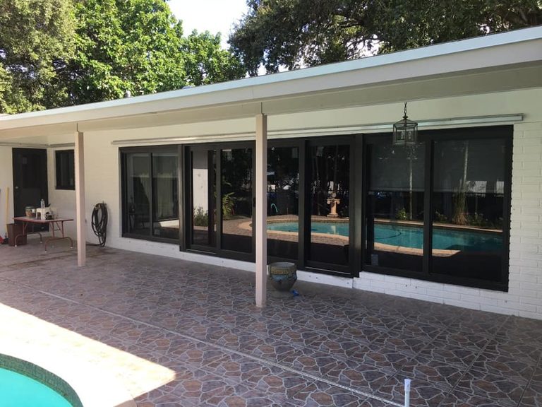 Black-framed sliding glass doors installed on a tiled patio next to a pool.