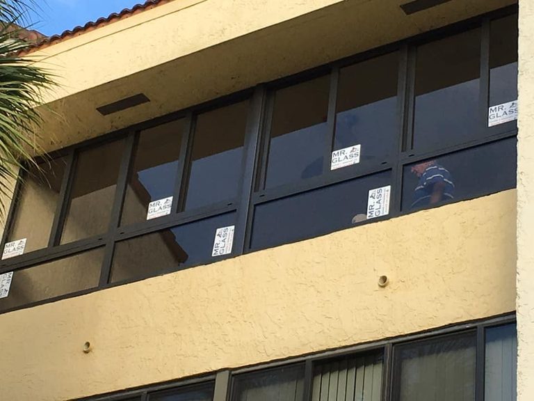 Exterior view of newly installed windows with manufacturer stickers on a stucco building.