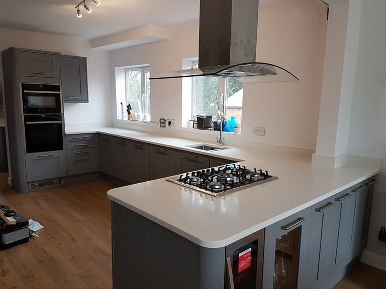 Modern kitchen with grey cabinets, white countertops, a gas stove on the island, and wood flooring.