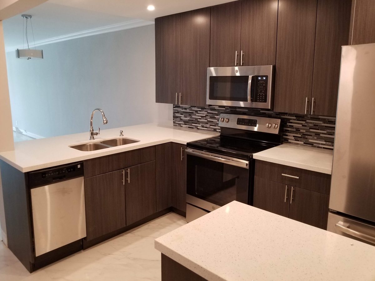 Modern kitchen with dark wood cabinetry, white countertops, and stainless steel appliances.