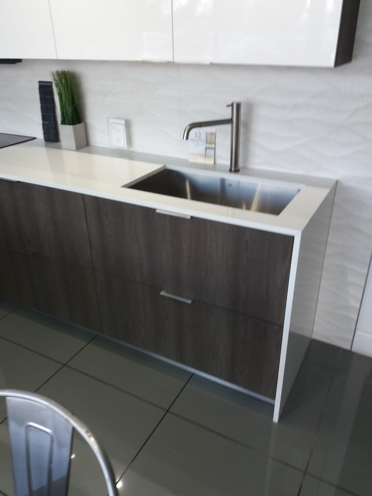 Modern kitchen counter with a stainless steel sink, white countertop, and dark wood cabinets.