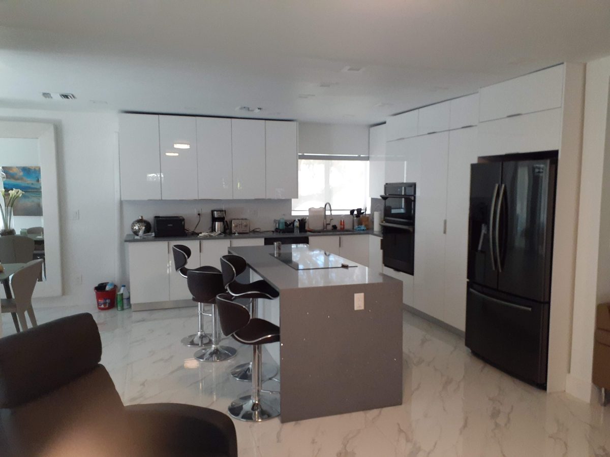 Modern kitchen with white cabinets, grey island, and marble tile floor.