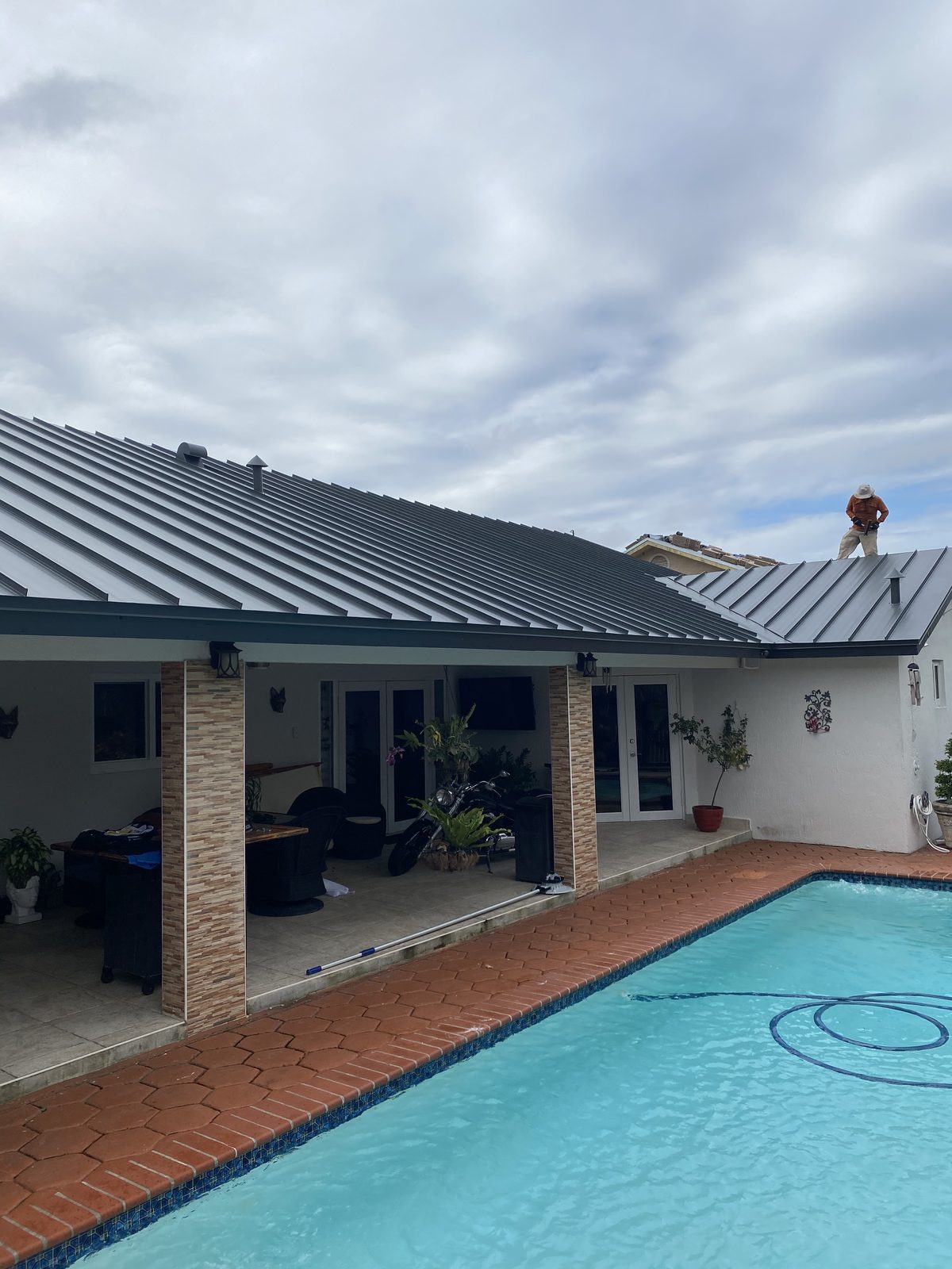 A newly installed dark metal roof on a house with a swimming pool.