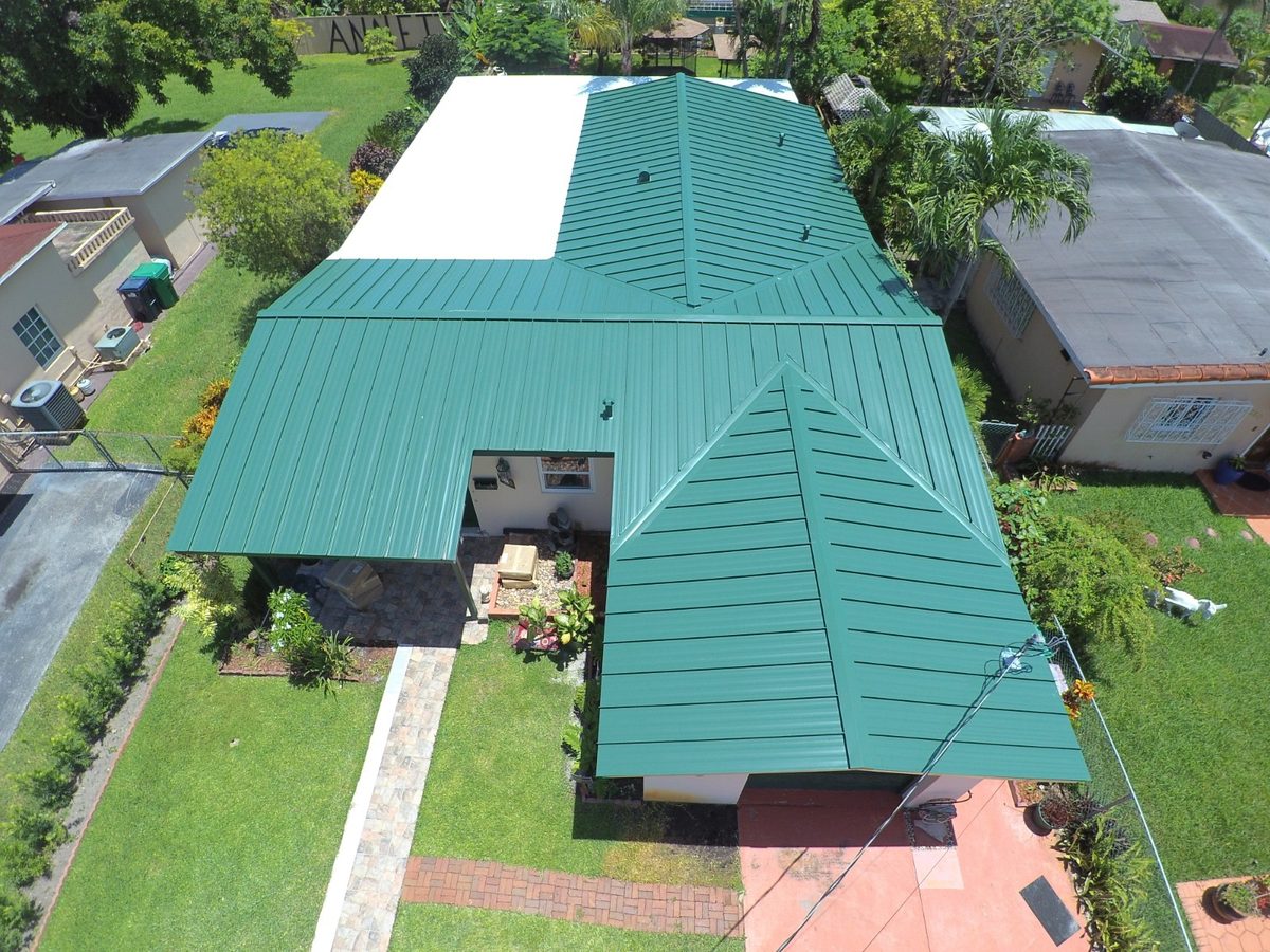 Aerial view of a house with a newly installed green metal roof and a white flat roof section.