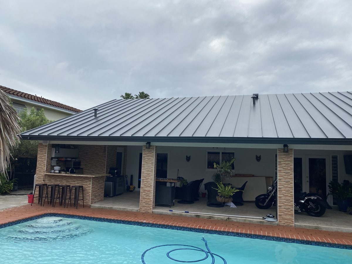 A newly installed grey metal roof on a house with a swimming pool in the foreground.