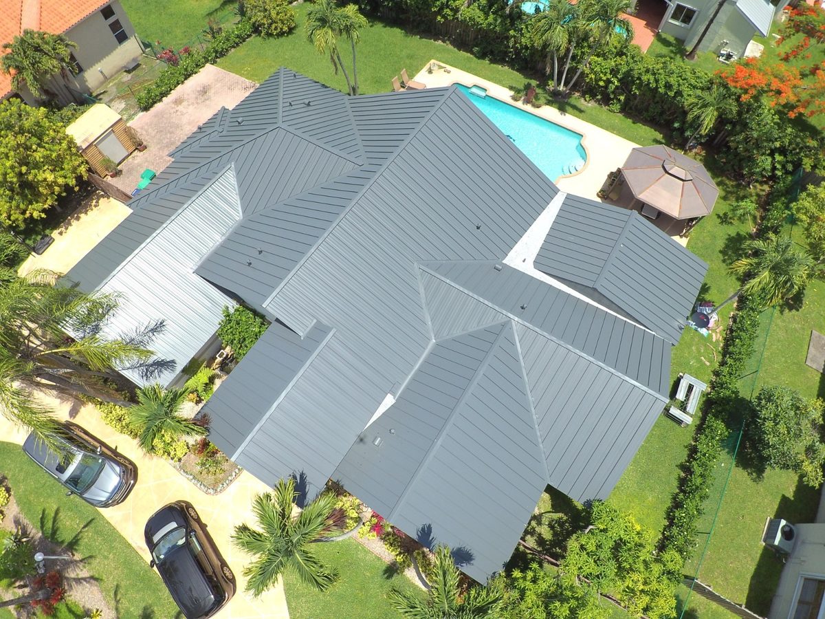 Aerial view of a residential home featuring a newly installed grey metal roof next to a swimming pool.