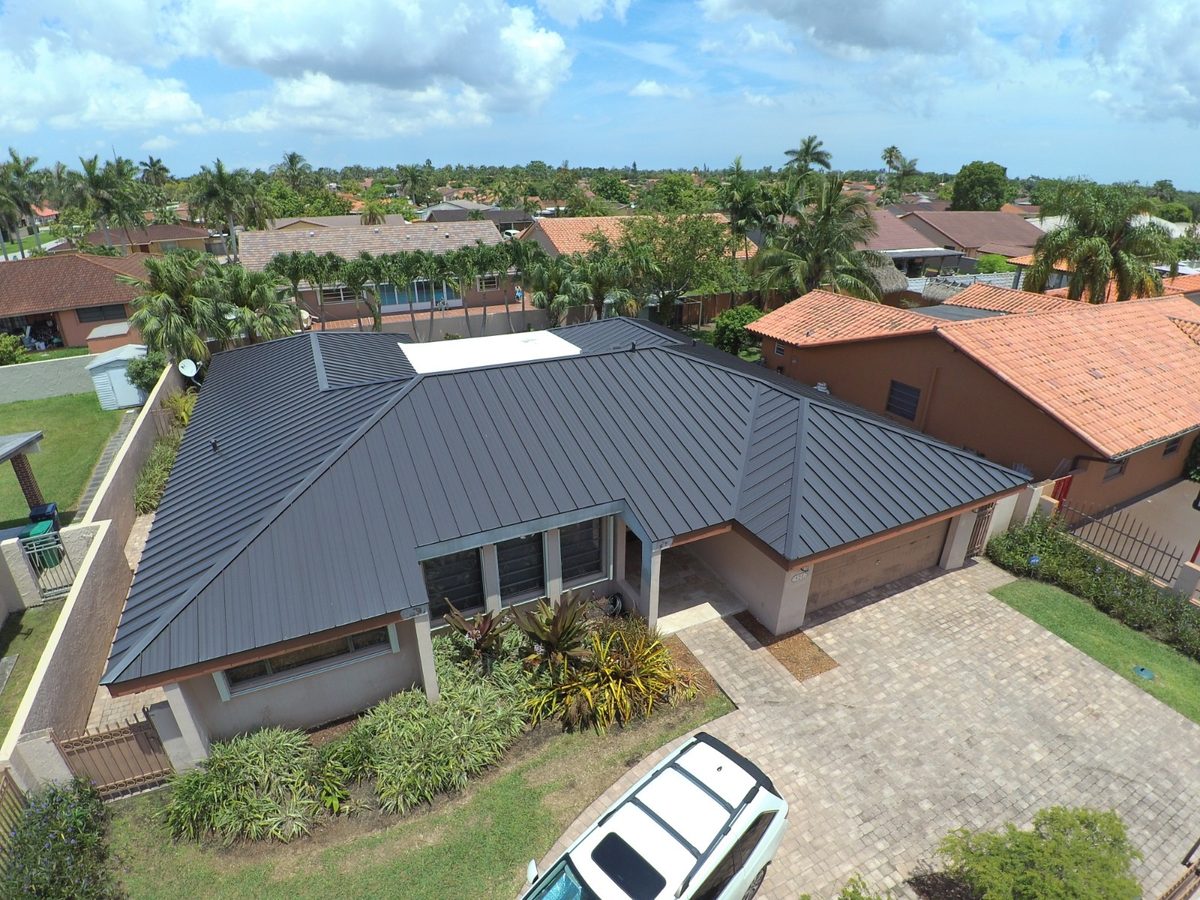 Aerial view of a house featuring a new dark gray metal roof and paved driveway.